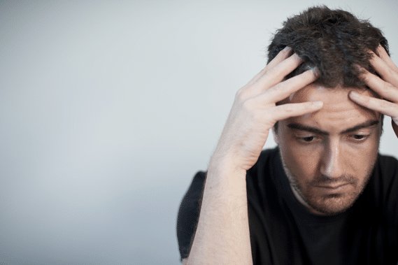 Depressed man looks down while hands on head