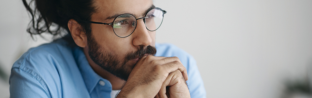 depressed or serious man with beard and round glasses sits thinking