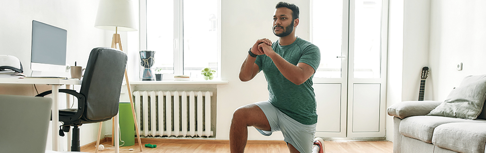 man in green tshirt and grey shorts doing squat at home online workout