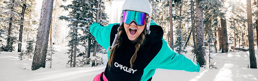 woman ski goggles white helmet teal jacket arms out wide in snowy forrest