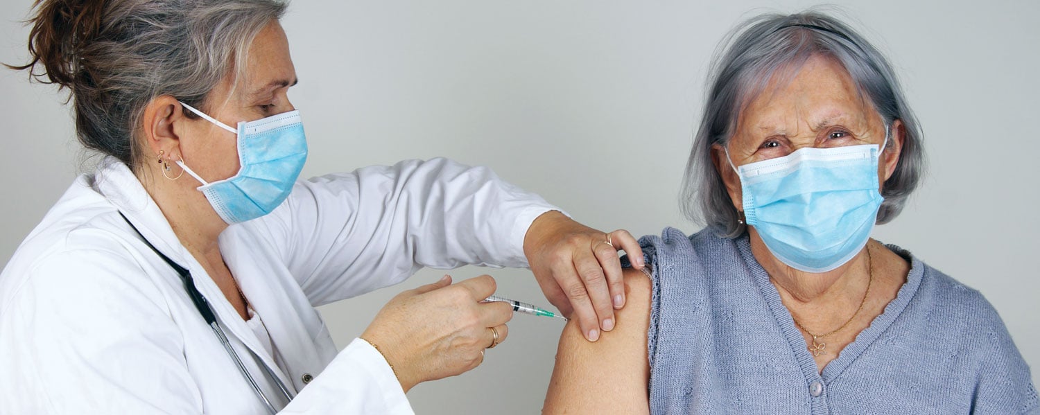 doctor giving vaccine shot to senior woman wearing masks