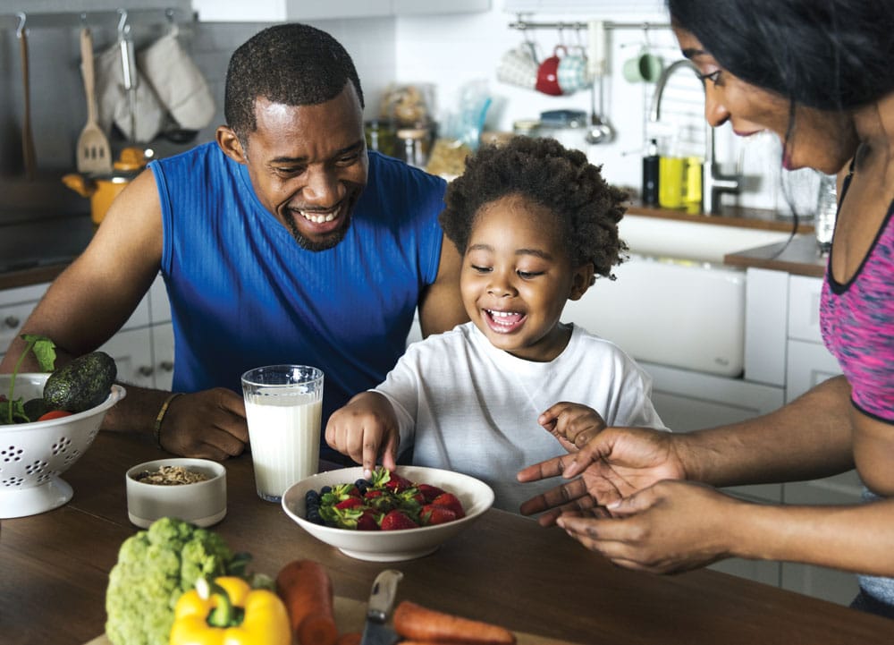 family eating bowl of strawberries in kitchen