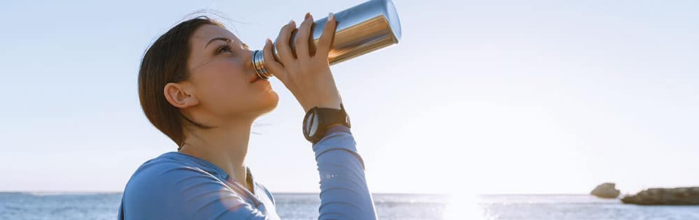 woman drinking from a water bottle near a lake