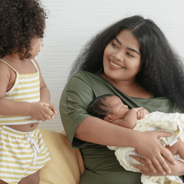 mom-long-hair-holding-newborn-smiling-at-toddler@2x