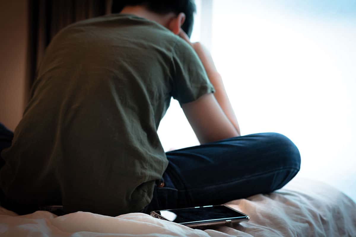 withdrawn, sad teen phone sitting behind him